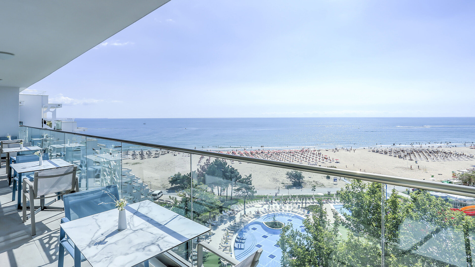 VIP Lounge Balkonterrasse mit Tischen, Glasgeländer und weitem Blick auf Strand, Meer und Resortpools