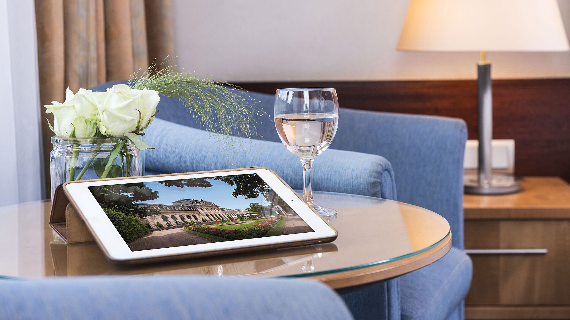 Gemütlicher Sitzbereich im Maritim Hotel Fulda mit Tablet, Glas Wasser und weißen Rosen auf einem Glastisch.