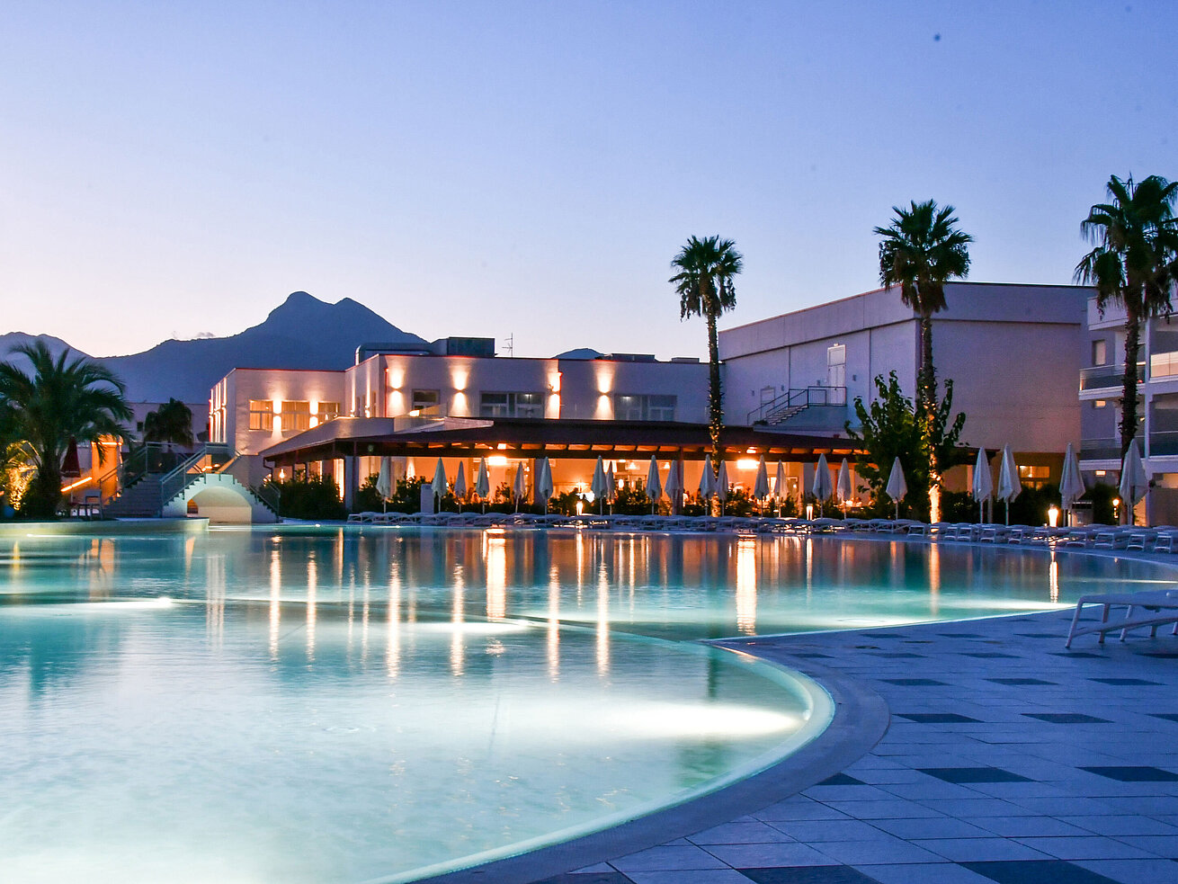 Luces nocturnas en la piscina del Maritim Resort Calabria con palmeras y montañas