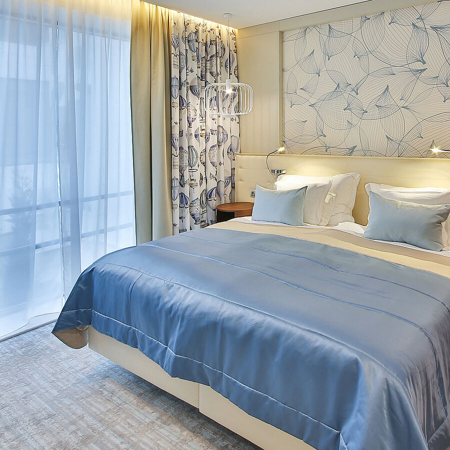 Apartment Modernes Hotelzimmer mit Doppelbett, blauen Akzenten und großen Fenstern mit Vorhängen