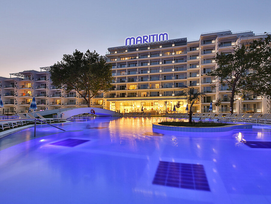 Beleuchtetes Maritim Hotel bei Sonnenuntergang mit großem Pool, Liegen und einladender Abendatmosphäre